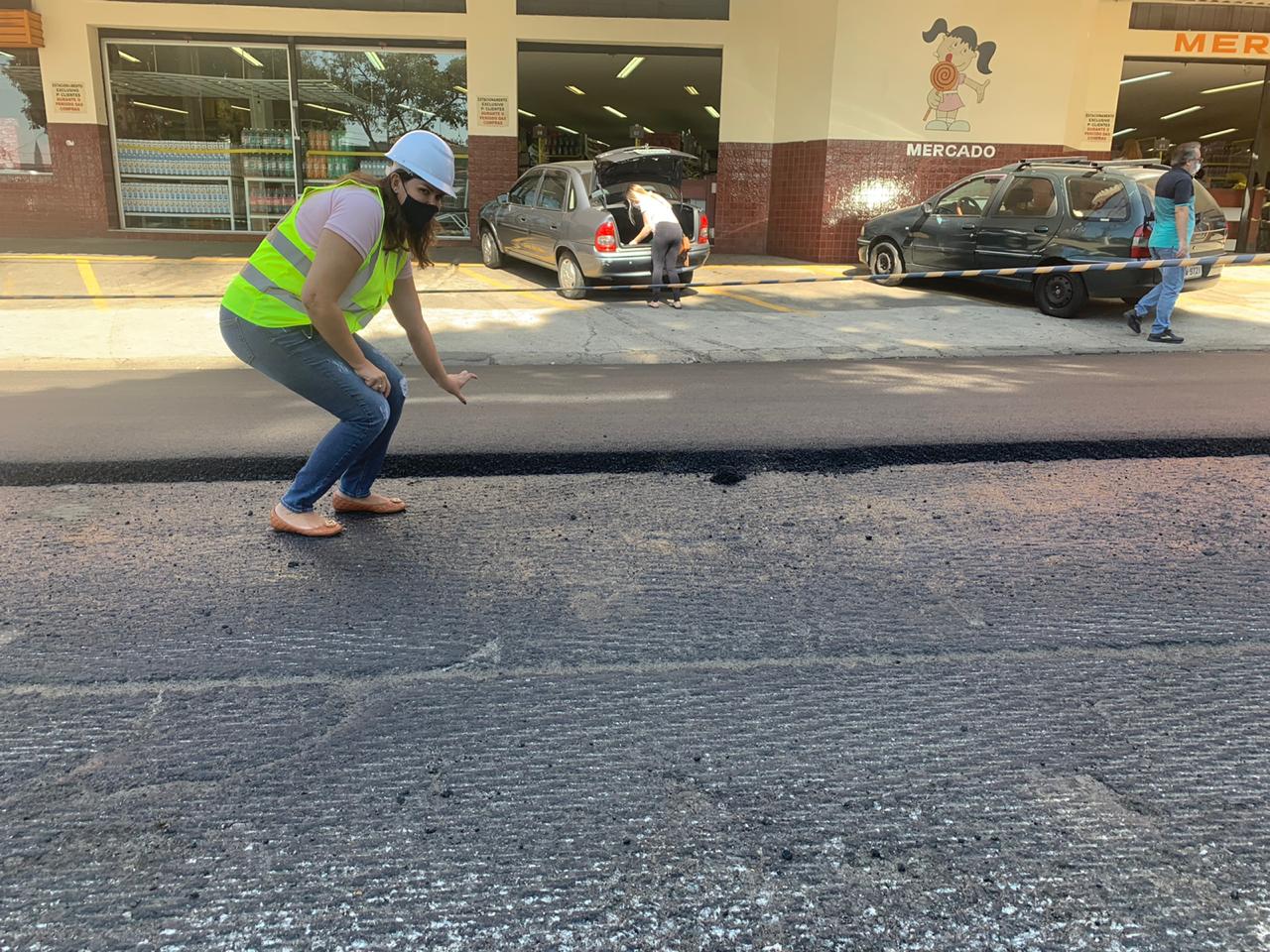 A Foto mostra a Subprefeita fernanda galdino vestida com colete,  capacete e mascara sinalizando o tamanho da massa asfáltica colocada no recapeamento